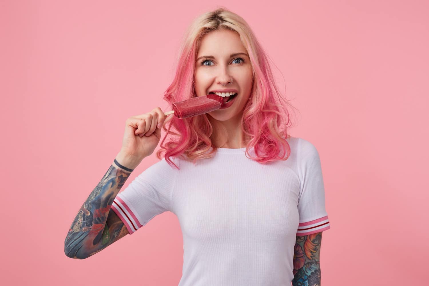 portrait-young-beautiful-pink-haired-girl-with-tattooed-hands-wearing-white-t-shirt-looking-trying-bite-off-ice-cream-standing